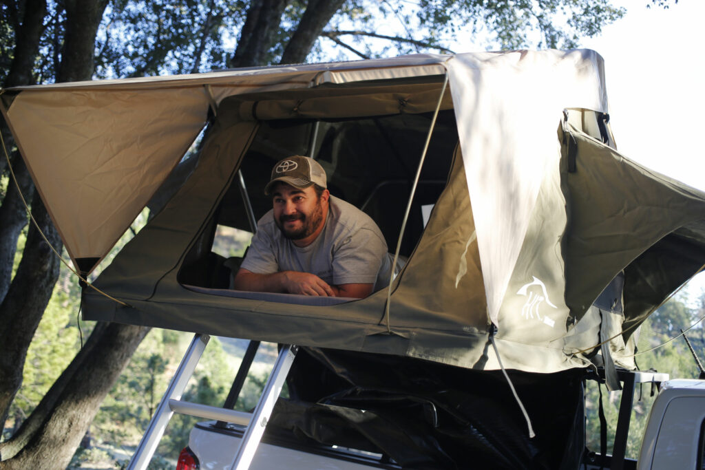 An outdoor guy feels satisfied while inside his car rooftop tent.